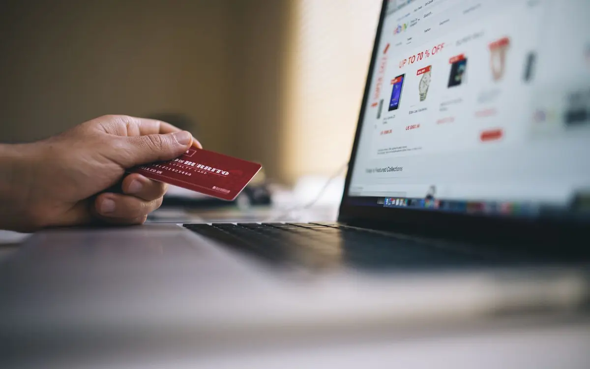 Carte bancaire tenue devant un ordinateur lors d'un achat sur une boutique en ligne